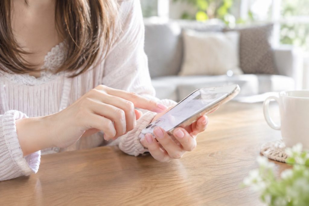テーブルでスマートフォンを操作する女性の手元のイメージ