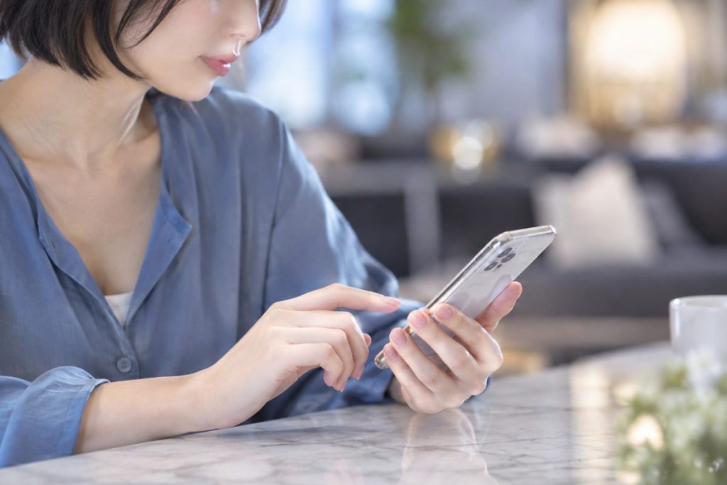 窓辺のテーブルでスマートフォンを見る女性のイメージ