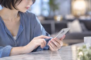窓辺のテーブルでスマートフォンを見る女性のイメージ